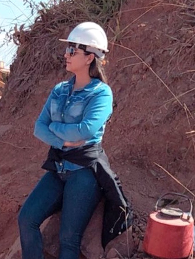 Eng. Gabriela Miranda em campo, com capacete de segurança, durante uma obra de terraplenagem